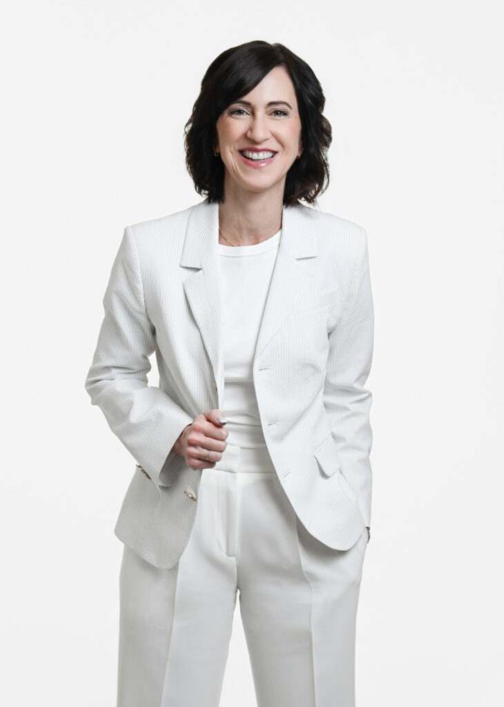 Corporate headshot of a female professional wearing a white suit against a white background