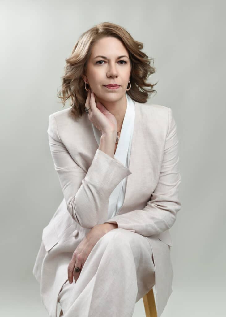 Woman in cream tailored suit seated with hand near chin, confident professional expression — Ellahrika Photography personal branding portrait, Milton, Ontario